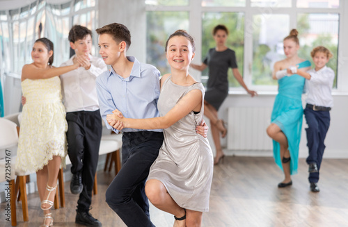Cheerful emotional teenagers in formal wear practicing modern vigorous dance movements at group lesson in choreography studio..
