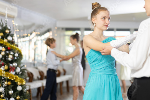 Smiling teenage girl enjoying slow dance with friend at school event during festive Christmas party with group of peers..