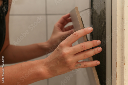 Woman tiling bathroom walls, applying adhesive on a tile and placing ceramic tile in right position. Process of installation of tiles in the bathroom step by step. DIY home improvement.