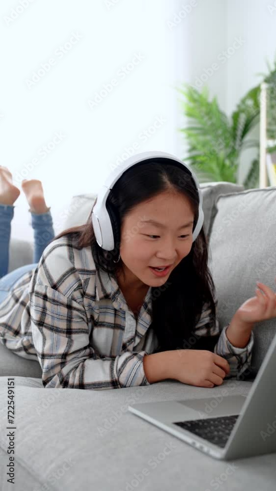 Young asian pretty woman having video call on laptop while lying on sofa.