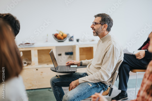 Canvas Print Engaged man in casual attire interacts with team members at an informal business meeting, laptop in hand