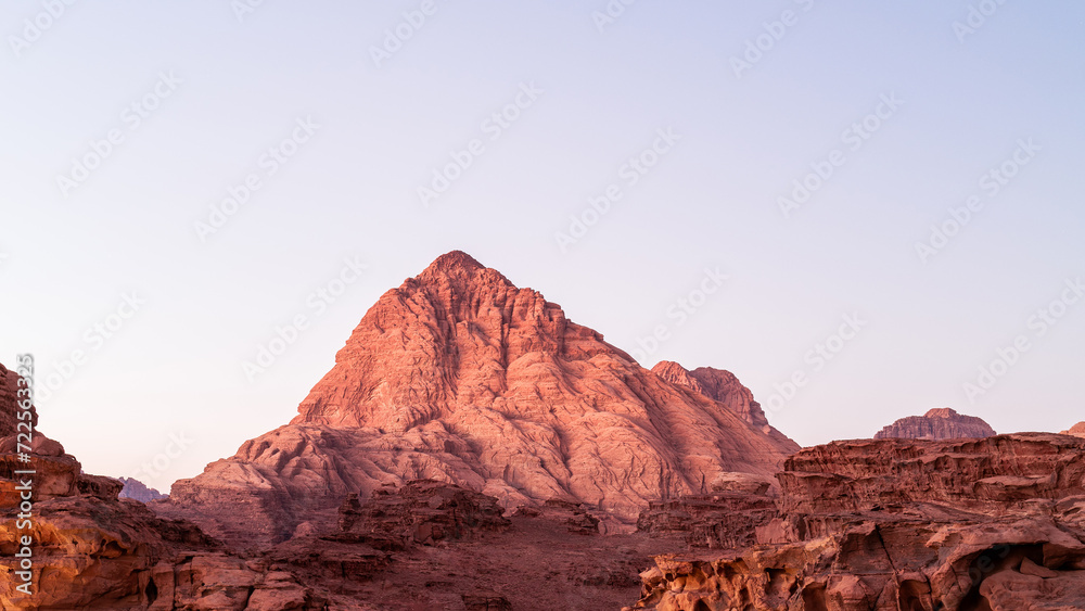 Wadi Rum, Jordan, the sun sets over a mountain with serene scenic vista, pink and red tones with blue sky. Scenery looks like Mars Wadi Rum, Jordan, the sun sets over a mountain with serene scenic vista, pink and red tones with blue sky. Scenery looks like Mars