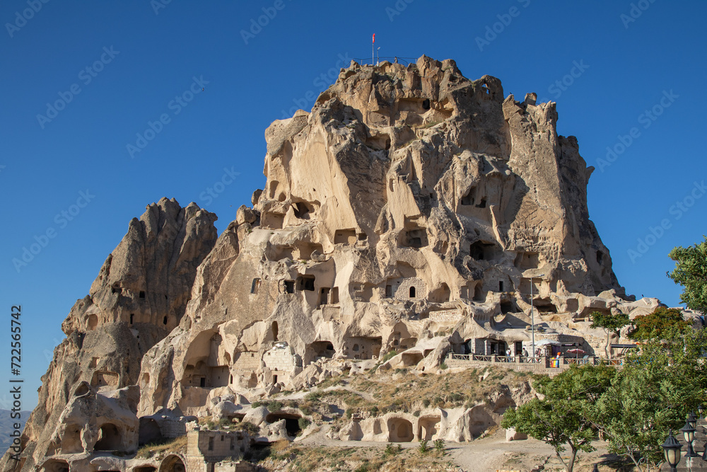 Ancient rock castle in Cappadocia, Turkey, with intricately carved cave rooms, set against a clear blue sky, perfect for historical and travel themes.