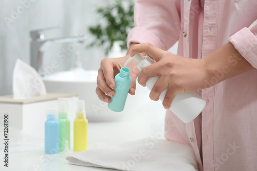 Woman pouring cosmetic product into plastic bottle over white countertop in bathroom, closeup and space for text. Bath accessories