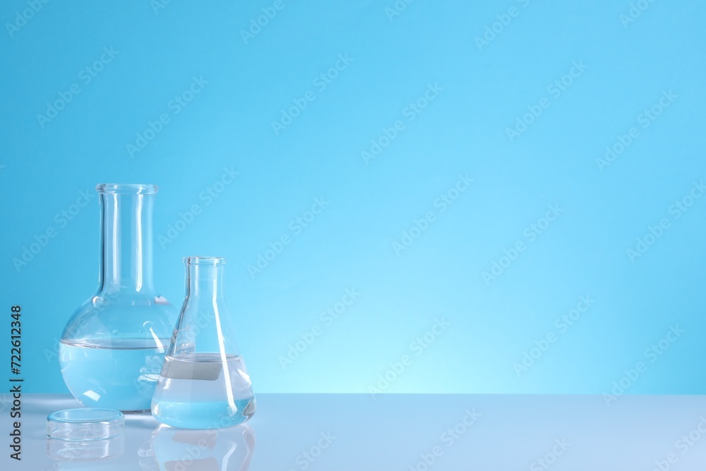 Laboratory analysis. Glass flasks on table against light blue background, space for text Laboratory analysis. Glass flasks on table against light blue background, space for text