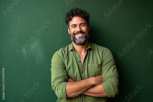 Portrait of a happy mature man standing with arms crossed against green chalkboard