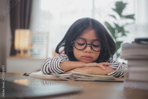 Little Asian girl sitting alone and looking out with a bored face, Preschool child laying head down on the table with sad bored with homework, spoiled child