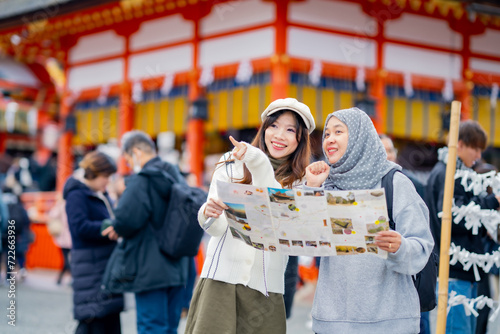 Travel, muslim, Two Asian female tourists of different religions friends visitor learning about history of fushimi inari shrine in travel book while walking through senbon torii path in Kyoto Japan.