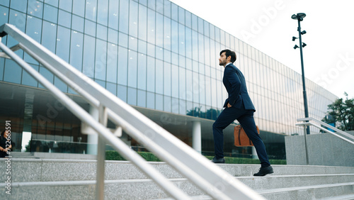 Skilled business man walking up stairs at park or city while holding bag in the hand Professional project manager going to workplace. Represent growth  getting promotion  increasing skill. Exultant.