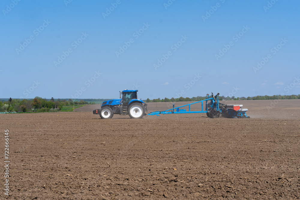 Obraz premium The tractor drives across the field and cultivates the land. Agricultural vehicle works in countryside. Sowing is the process of planting seeds in the ground as part of the early spring time