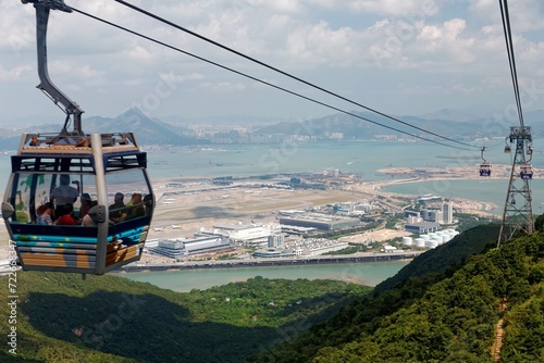 Tourists ride in a gondola of Ngong Ping Cable Car (Skyrail) gliding over the mountainside & enjoy the panoramic view of Hong Kong International Airport on Chek Lap Kok Island in Hongkong, China, Asia