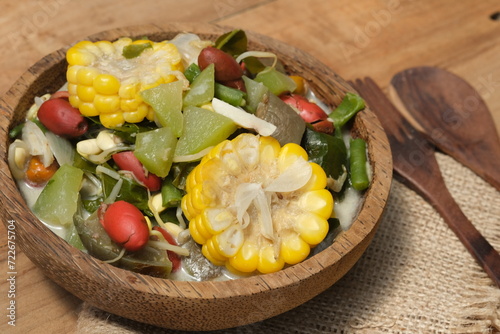 Sayur lodeh or vegetables with coconut milk soup is traditional Indonesian culinary food from Java in white bowl served on coconut tree trunk bowl, on a wooden table. Selective focus. Top view.  photo