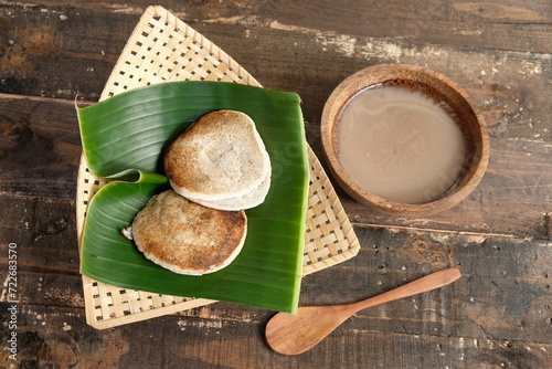 Serabi Surabi Kocor is traditional Javanese snack made of rice flour, coconut milk, pandanus leaves, and palm sugar. Served in bamboo woven basket on wooden table. Flat lay. Indonesian food.  photo