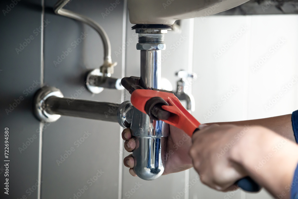 Plumber uses wrench to repair water pipe under sink There is maintenance to fix the water leak in the bathroom.with red wrench, plumbing install concept. - obrazy, fototapety, plakaty 