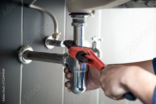 Plumber uses wrench to repair water pipe under sink There is maintenance to fix the water leak in the bathroom.with red wrench, plumbing install concept. photo