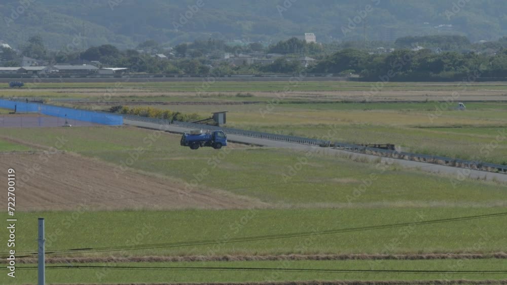 Truck driving on a rural road next to rice paddies with mountains in the background, daytime Truck driving on a rural road next to rice paddies with mountains in the background, daytime