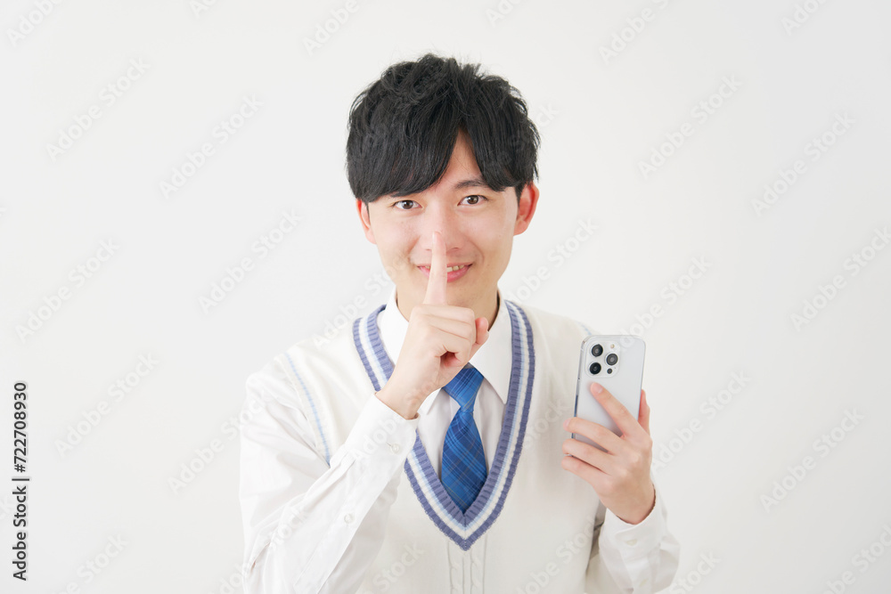 スマートフォンを持って内緒のポーズをする男子高校生　白背景