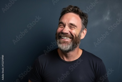 Handsome middle aged man with beard and mustache laughing against a blue chalkboard