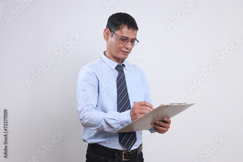 Adult Asian businessman wear glasses and formal clothes writing on clipboard