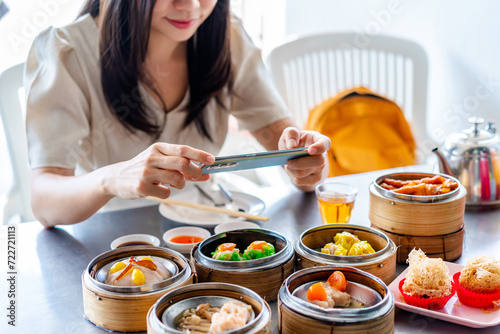 Young woman traveler taking a photo of traditional Chinese Dim Sum at restaurant while traveling