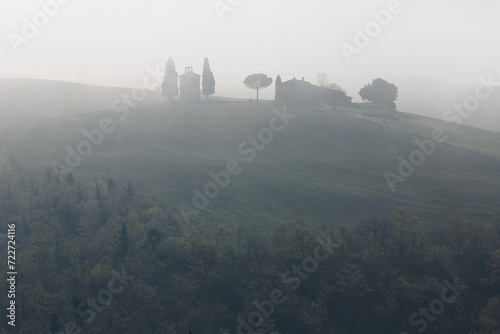 Beautiful scenery of Chapel Vitaleta on a hilltop in idyllic Tuscan countryside with rolling hills veiled in morning fog in an ethereal mysterious atmosphere, in Pienza, Val d'Orcia, Tuscany, Italy