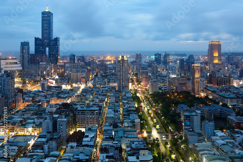 Aerial view of Kaohsiung City at dusk, a vibrant seaport in South Taiwan, with the famous landmark 85 Sky Tower standing by the harbor in background and street lights dazzling in blue evening twilight