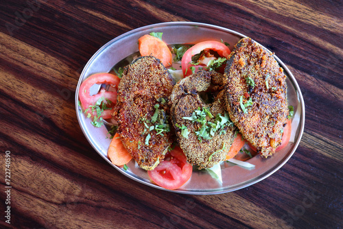 Indian king fish fry. Surmai Rava fry. also known as talaleli Surmai in Marathi. served with onion and tomatoes placed over a rustic wooden background, selective focus. Copy space. photo