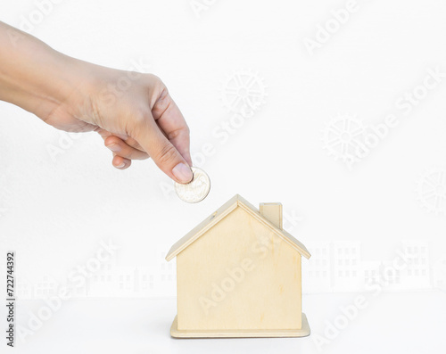 Hand holding coin with house piggy bank on white background with gear and builiding pattern background, saving money, property investment photo