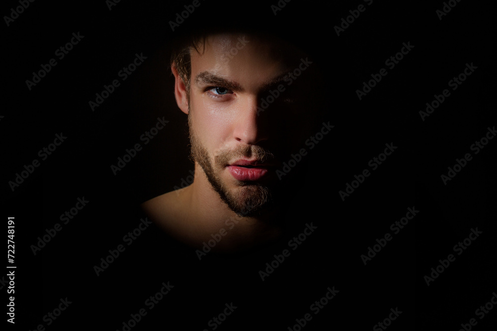 Sexy gay studio portrait. Silhouette portrait of a young man. Man in shadows. Upper body man silhouette. Black studio background. Young man close-up portrait, with shadow on studio lowkey. Studio shot