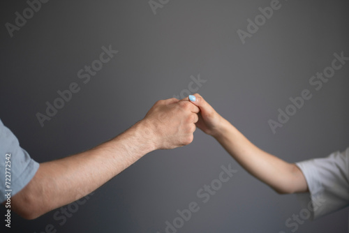A close-up view captures the tender touch between a mans and a womans hand against a neutral gray backdrop.