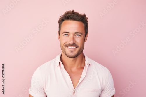 Portrait of handsome young man looking at camera with smile while standing against pink background