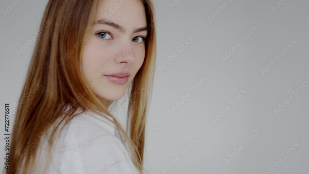 Blonde young woman in loose shirt poses for camera in photo studio with gray background. Young model demonstrates emotions of happiness and confidence during photo session. Photo posing