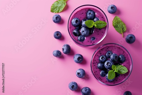Two glasses of blueberries smoothie on pink background. Poring from blender into glass.