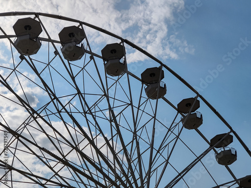 Part of large Ferris wheel against the background of summer daytime blue sky with clouds. Empty booths, no people. Attraction. Entertainment. Pastime. Vacation. Tourism. Copy space. Selective focus.