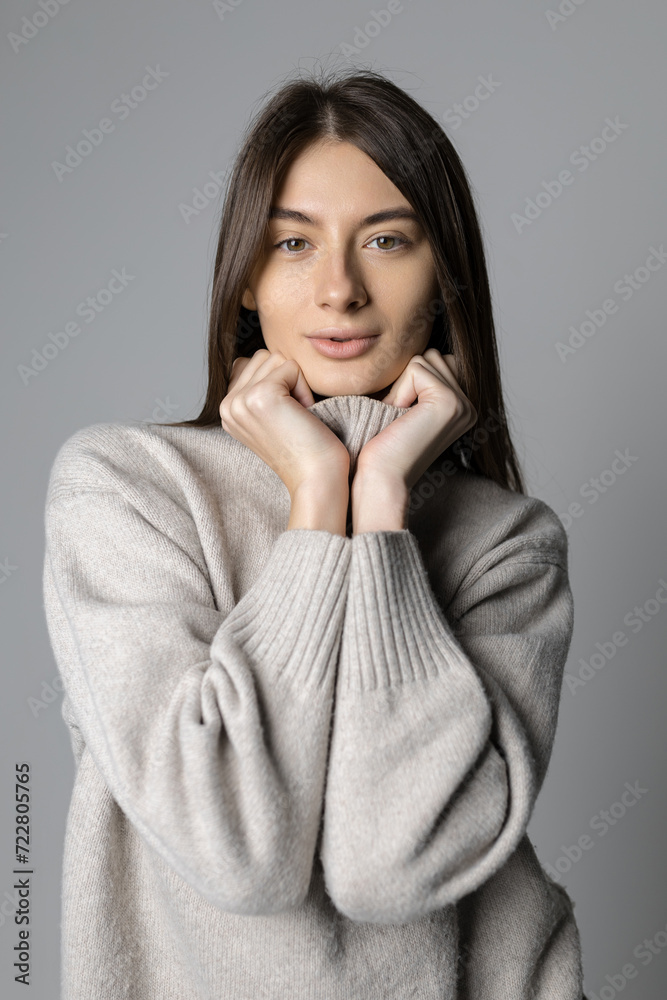 Portrait of a young woman without makeup in the studio. Stylish sweater on the model. Grey background