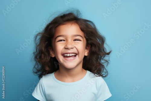 Portrait of a happy little girl with long curly hair smiling at the camera on a blue background