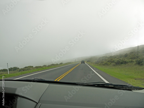Cars driving by windy road on the mountain slope covered with low clouds to the Haleakala Volcano peak on Maui, Hawaii