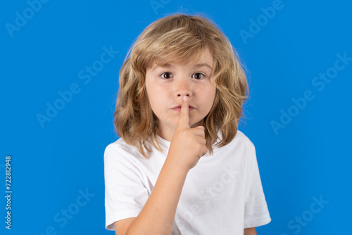 Kid with show no talk gesture. Boy with shows shh sign. Be quiet. Hush dont tell. Child put finger to lips mouth, ask stop share rumor, isolated over studio isolated background.