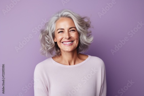 Cheerful mature woman looking at camera with smile while standing against purple background
