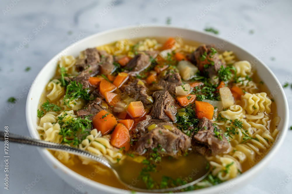 Clear beef soup or stew with noodles and root vegetables isolated on light background.