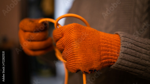 A hand's of a man in orange work gloves untangle orange wire. He wear Synthetic fiber closes