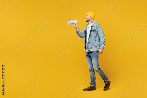 Full body young man he wears denim shirt hoody beanie hat casual clothes hold in hand megaphone scream announces discounts sale Hurry up isolated on plain yellow background studio. Lifestyle concept.