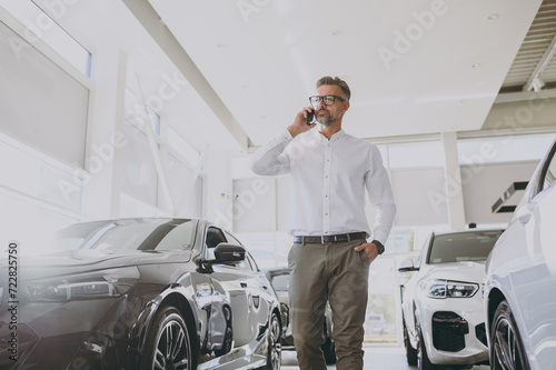 Adult rich man customer male buyer client wears shirt talk speak on mobile cell phone choose auto want to buy new automobile in car showroom vehicle salon dealership store motor show. Sales concept. © ViDi Studio