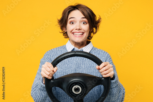 Young satisfied excited cheerful fun woman she wears grey knitted sweater shirt casual clothes hold steering wheel driving car isolated on plain yellow background studio portrait. Lifestyle concept.