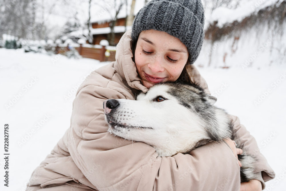 Smiling woman embracing husky dog on snow Smiling woman embracing husky dog on snow