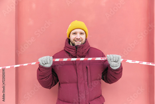 Happy man holding red and white barricade tape in front of peach wall