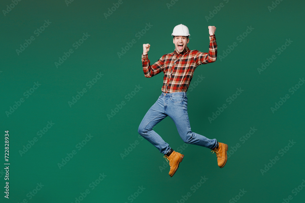 Full body young fun employee laborer handyman man wear red shirt hardhat jump high do winner gesture isolated on plain green background. Instruments for renovation apartment room. Repair home concept. Full body young fun employee laborer handyman man wear red shirt hardhat jump high do winner gesture isolated on plain green background. Instruments for renovation apartment room. Repair home concept.