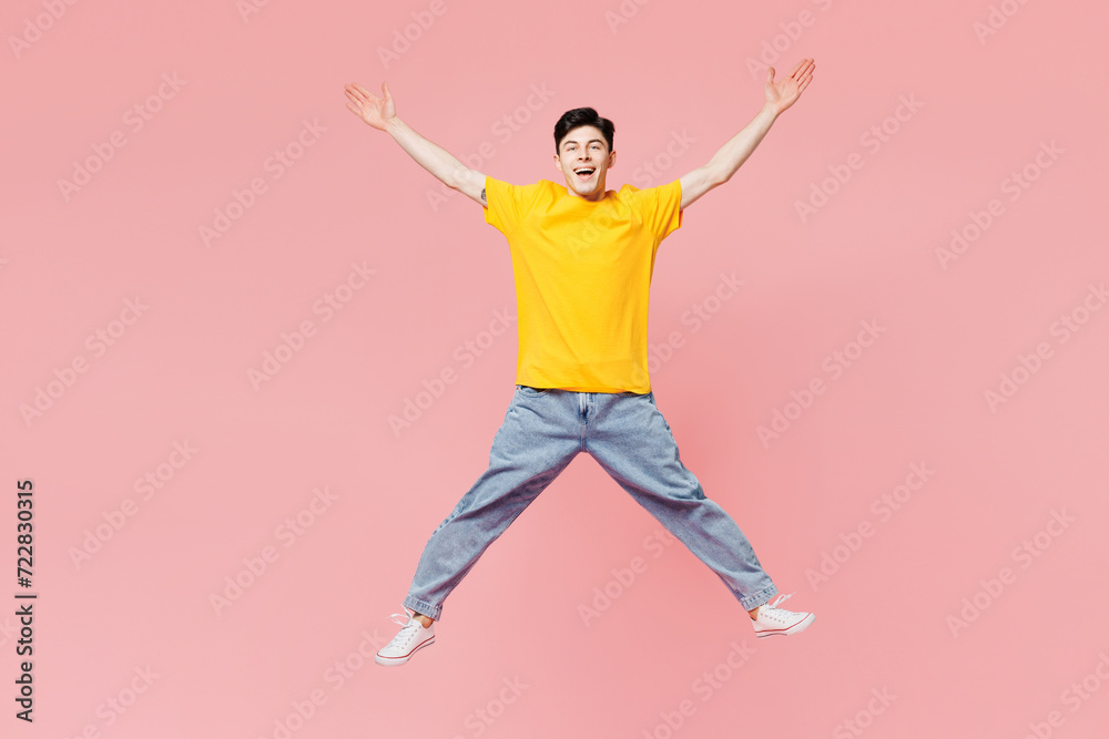 Full body young overjoyed fun man he wear yellow t-shirt casual clothes jump high with outstretched hands look camera isolated on plain pastel light pink background studio portrait. Lifestyle concept