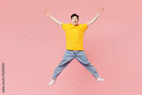 Full body young overjoyed fun man he wear yellow t-shirt casual clothes jump high with outstretched hands look camera isolated on plain pastel light pink background studio portrait. Lifestyle concept