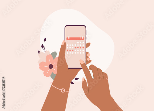 Black Female’s Hand Setting Dates On Monthly Calendar With Mobile Phone. Close-Up.